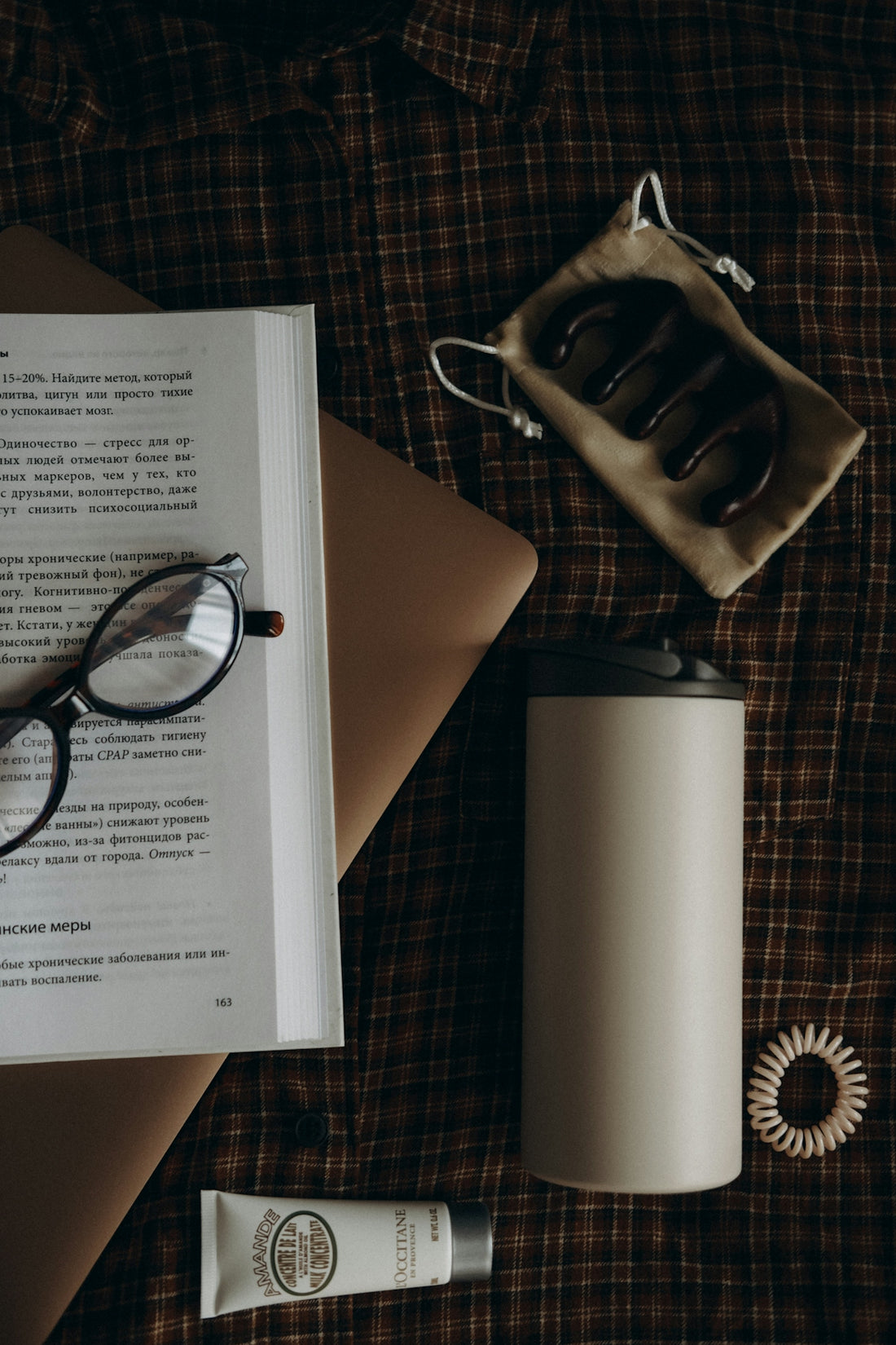 Book, glasses, and beauty products on plaid fabric